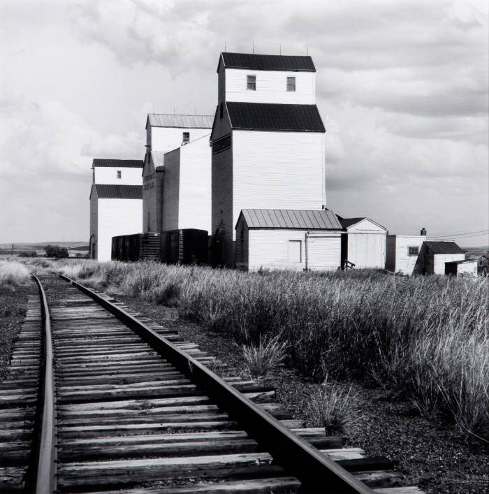 Photograph of railroad track on the left and grain elevators on the right.